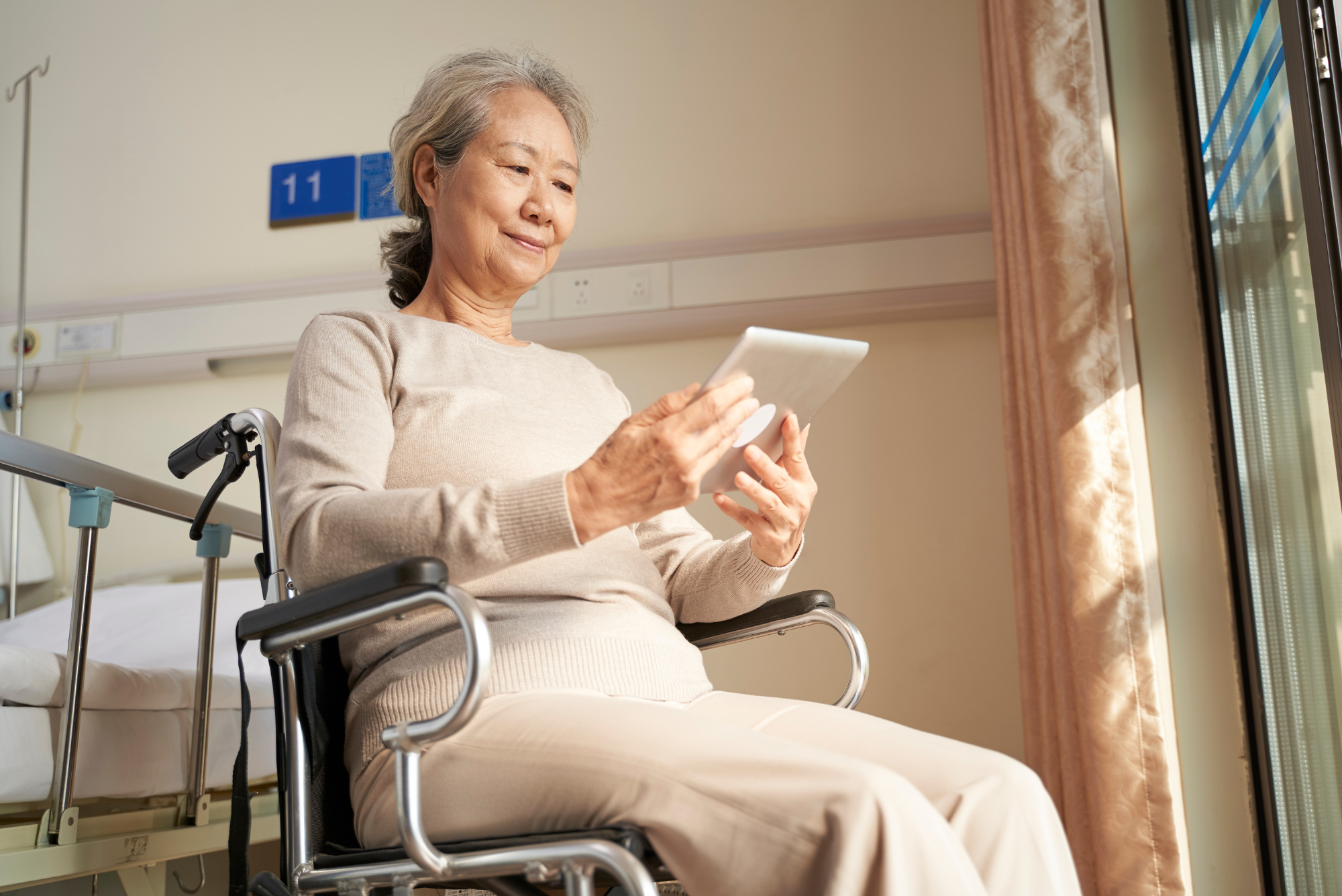 An older woman in a wheelchair smiles as she uses a helpful digital patient engagement platform to easily fill out a form.