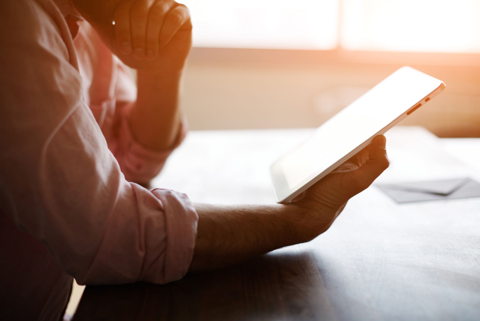 At sunset, a doctor with his hand on his chin considers different digital patient intake solutions on his tablet.