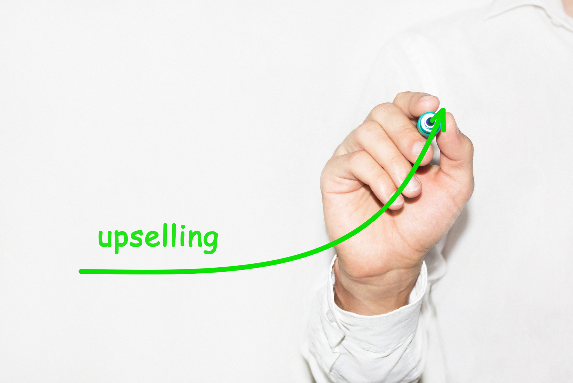 A man in a white dress shirt draws a green arrow, trending upwards, that is labeled “upselling,” symbolizing examples of upselling and cross-selling.