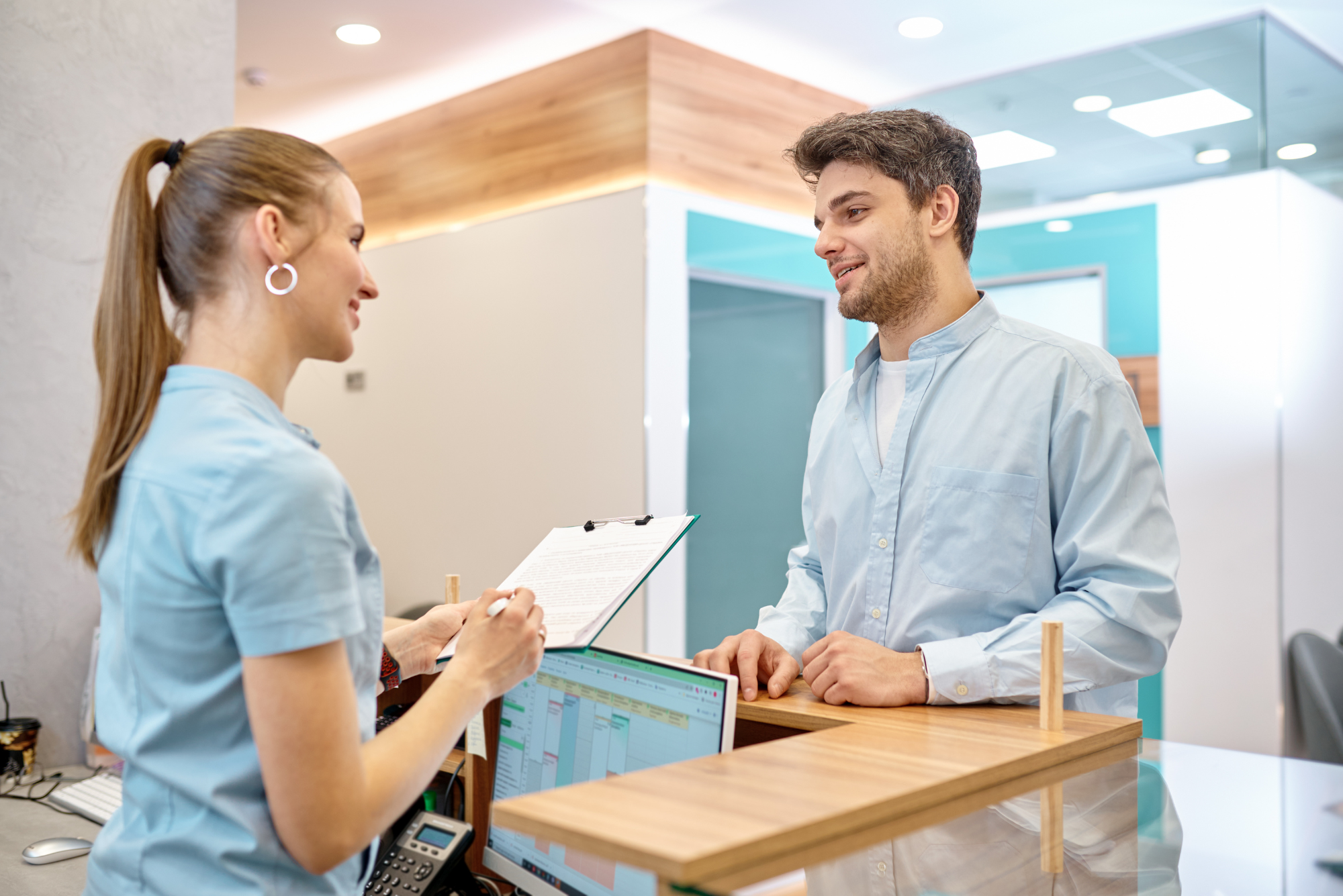 A receptionist hands a patient a clipboard with paper intake forms because her office needs a new front office automation solution.